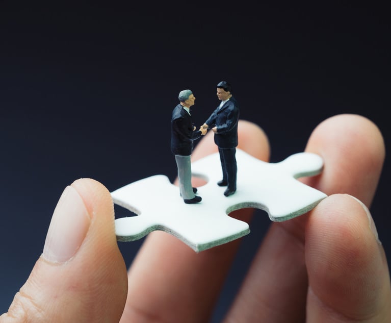 Two miniature businessmen shaking hands on a puzzle piece being held by a human hand.