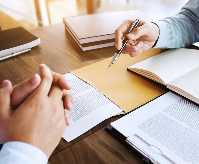 A close-up of the hands of two business people discussing something across a desk. There are books open between them.