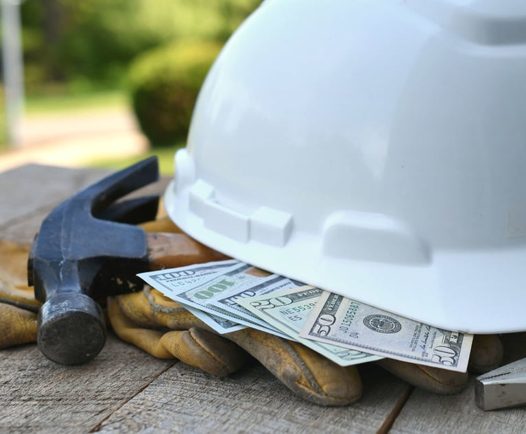 A hard hat sitting on top of a pile of money, a hammer and some work gloves.