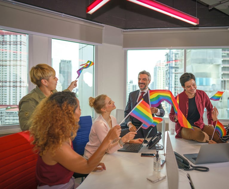 A group of people sitting in an office holding rainbow flags.